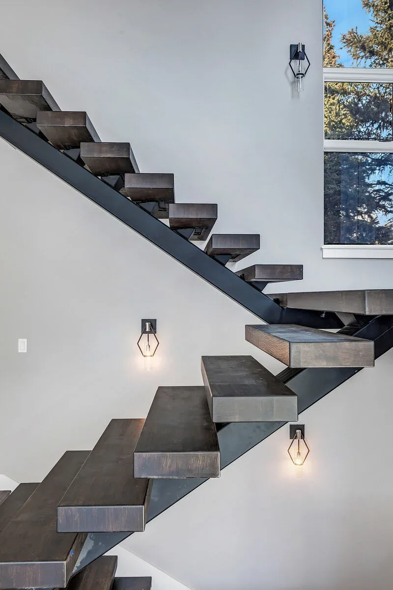 Floating stairs with dark wood treads and black metal stringers illuminated by geometric wall sconces beside a window.