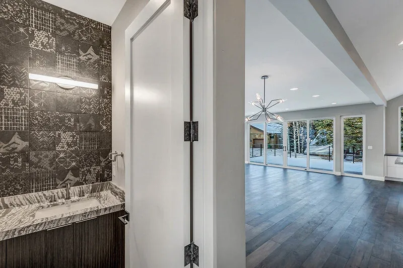 An open dining and kitchen space features large rectangular windows with snowy landscape views and a dark stone backsplash in the bathroom area.