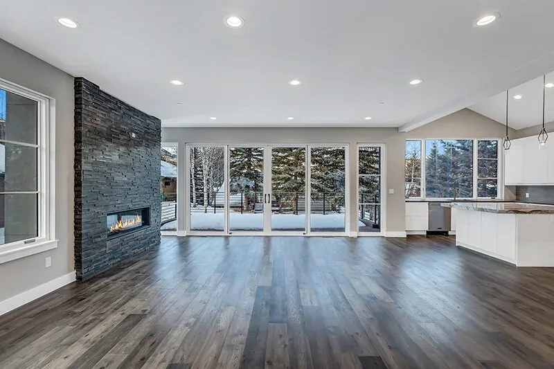The open living and kitchen area features a black stone wall with a linear fireplace and large glass sliding doors to the snowy deck.