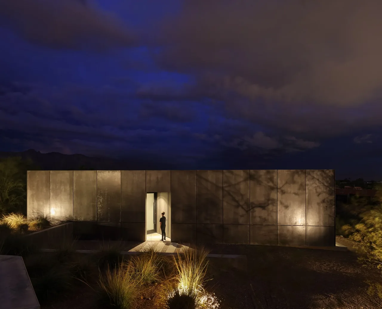 The casita OBSCURA features a minimalist design with a dark metal panel facade, highlighted at night by subtle lighting.