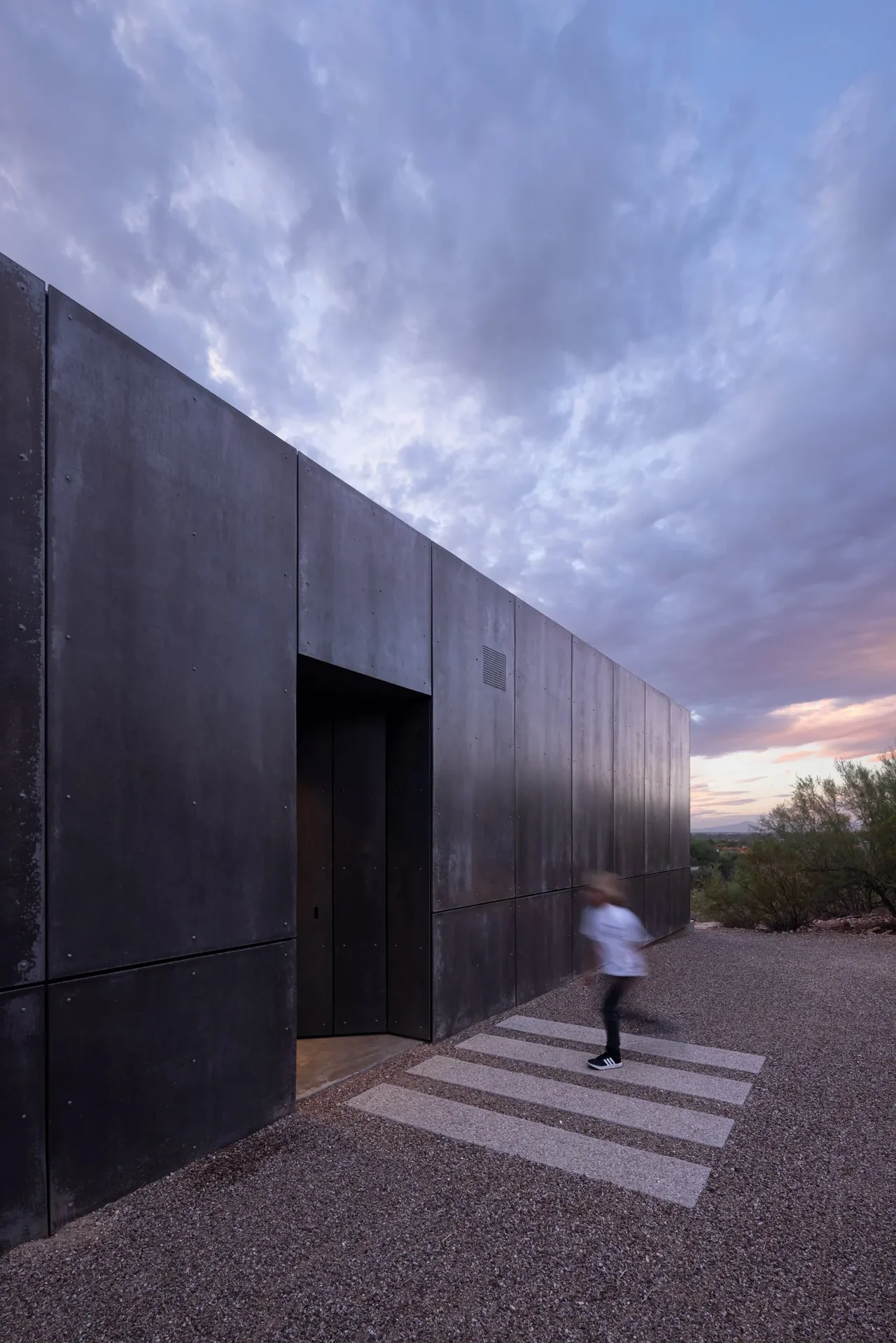 casita OBSCURA features a dark metal paneled exterior wall with a recessed entry under a cloudy twilight sky.
