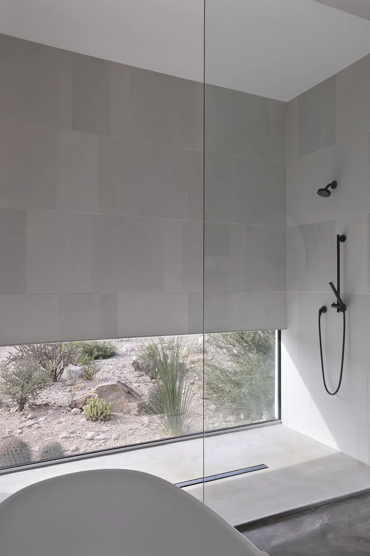 Shower area with matte black fixtures and floor-to-ceiling glazing showcasing a desert landscape view.