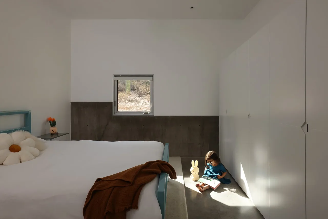 Minimalist bedroom with a small window, concrete wainscoting, and built-in white wardrobes.