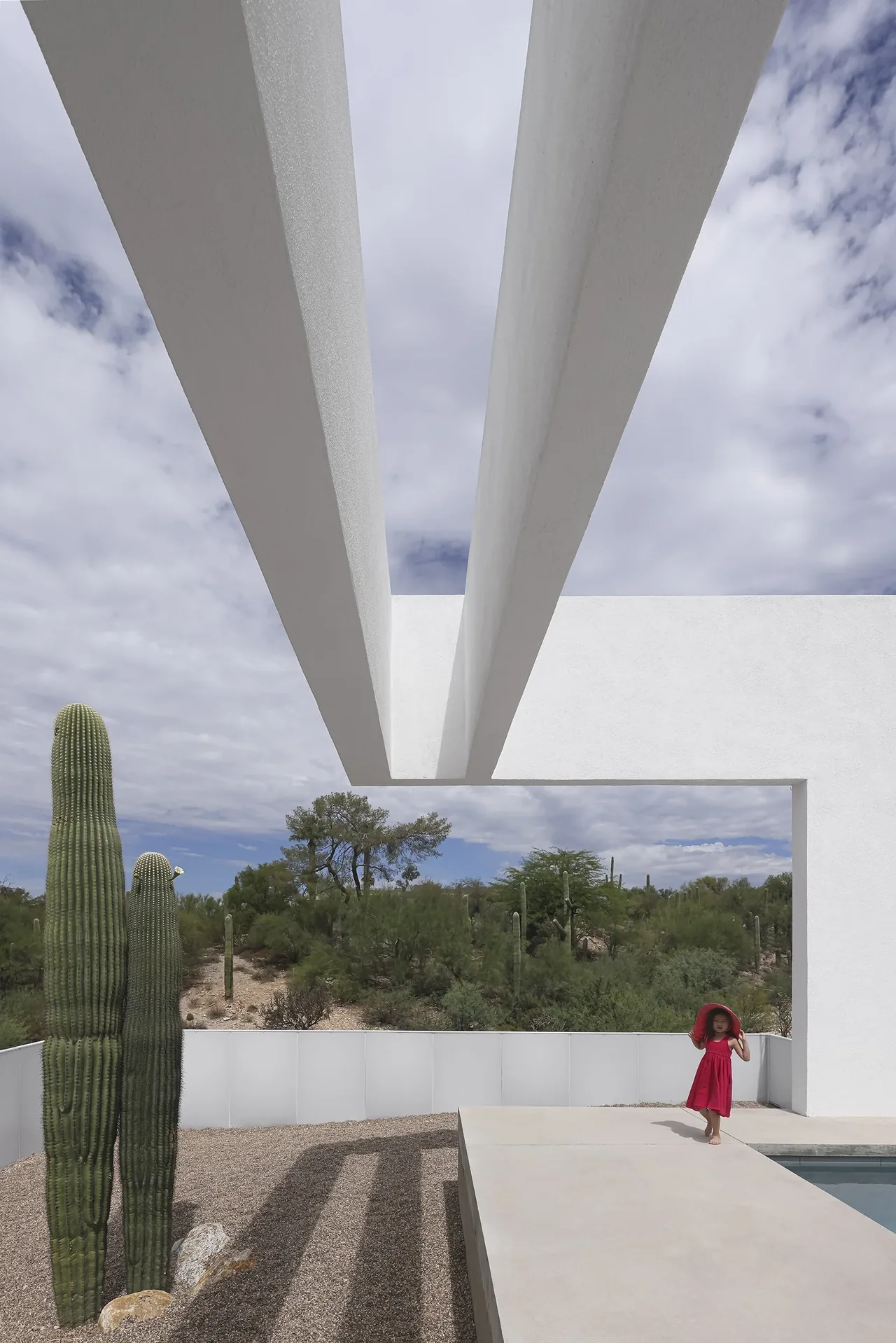 Modern minimalist outdoor pool area with white beams and desert vegetation seen in the background.
