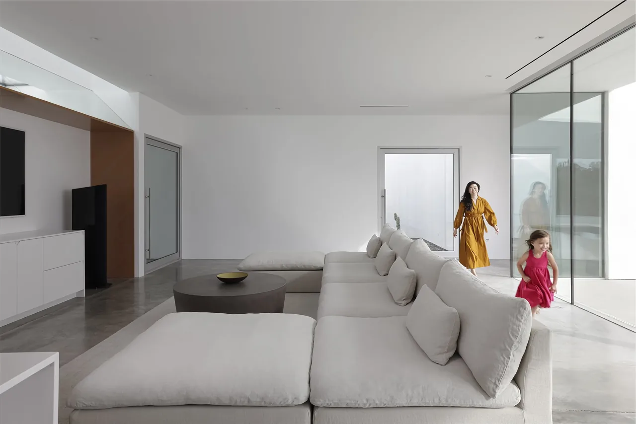 Inside a modern living room featuring a large white sectional sofa on polished concrete flooring with glass sliding doors.