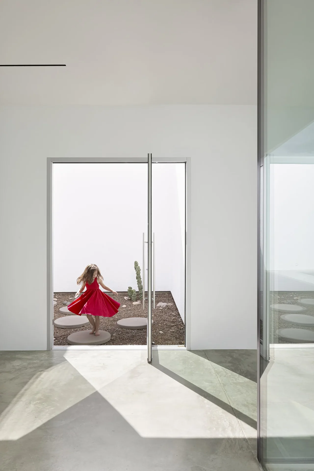 Minimalist courtyard with round concrete stepping stones and a large glass door opening to an indoor space with polished concrete floors.