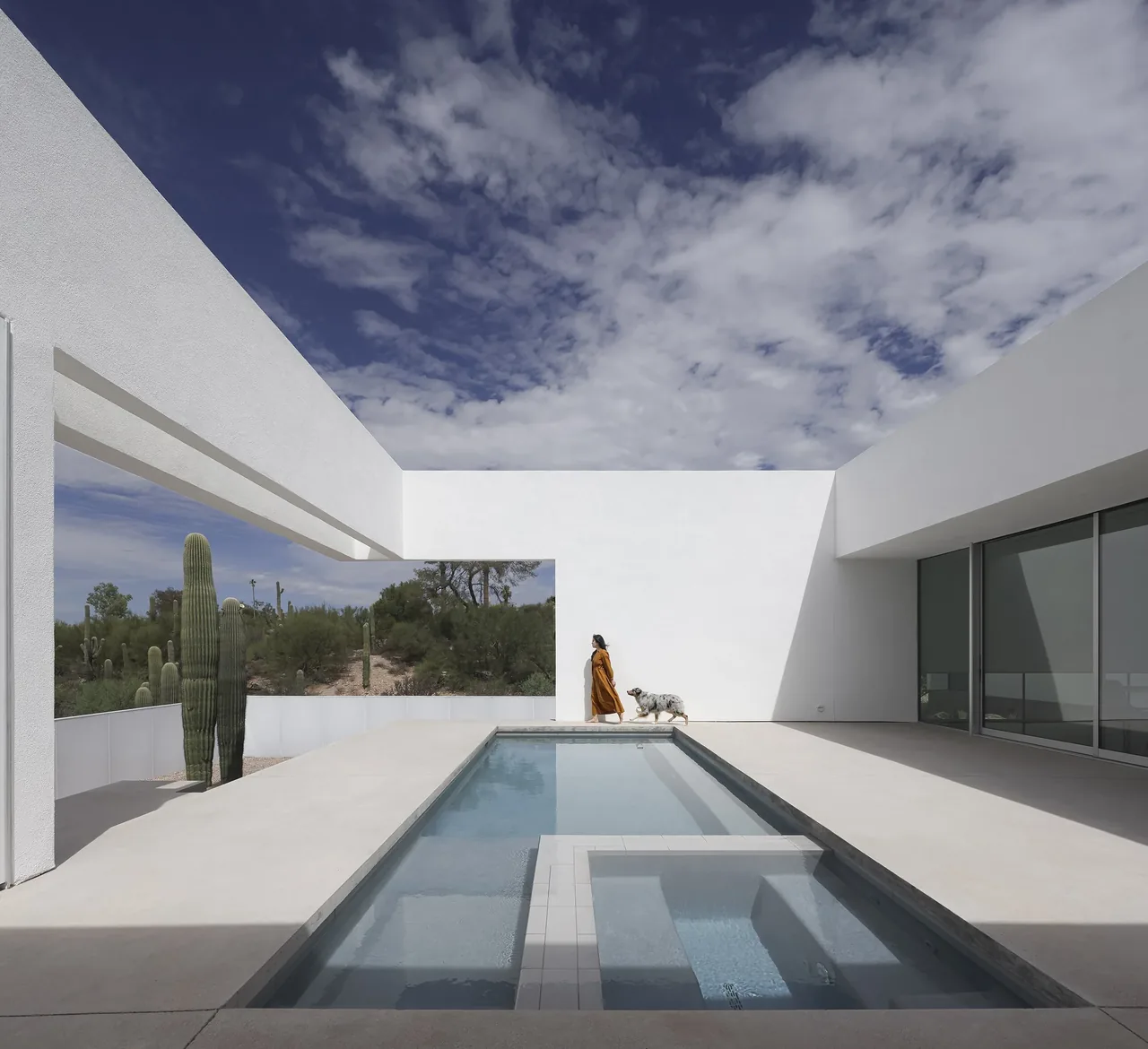 A minimalist outdoor pool courtyard in a desert landscape with stark white walls and clear skies.