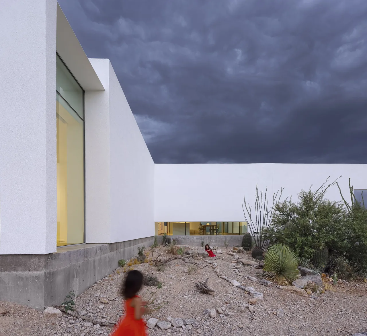 Modern house exterior with white walls and desert landscaping under dramatic clouds.