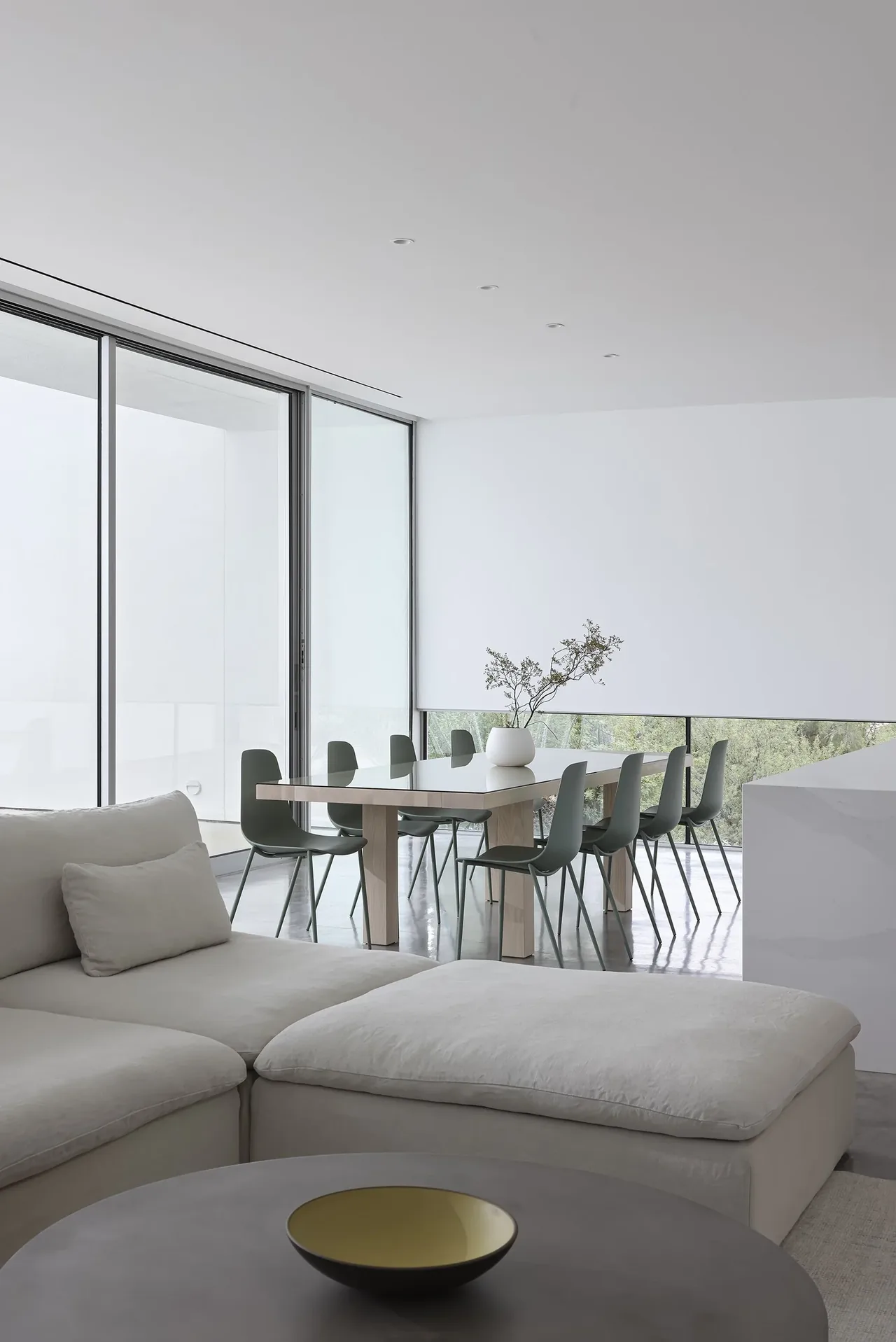 Dining area features a wood table with green chairs next to large floor-to-ceiling windows and a white sectional sofa.