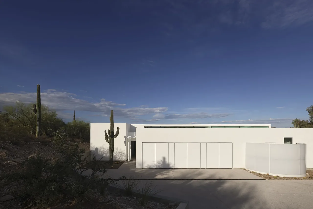 The real house by HK Associates features a minimalist white facade set in desert landscaping with flat roof design.