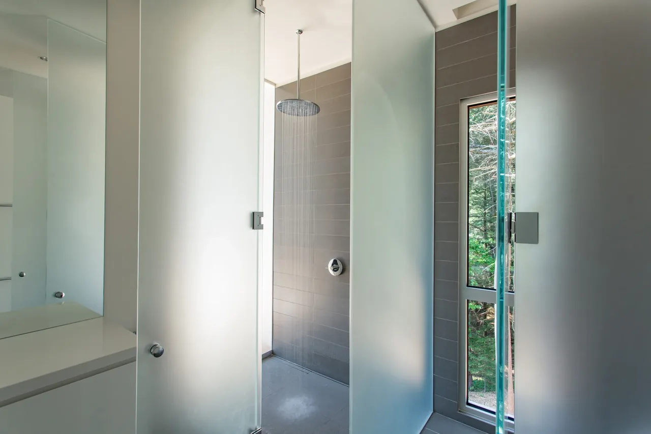 Shower room with frosted glass doors, rain shower, and vertical window overlooking natural landscape.