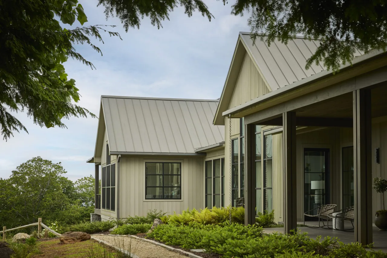 Modern farmhouse exterior with standing seam metal gable roofs and vertical wood siding in a natural landscape.