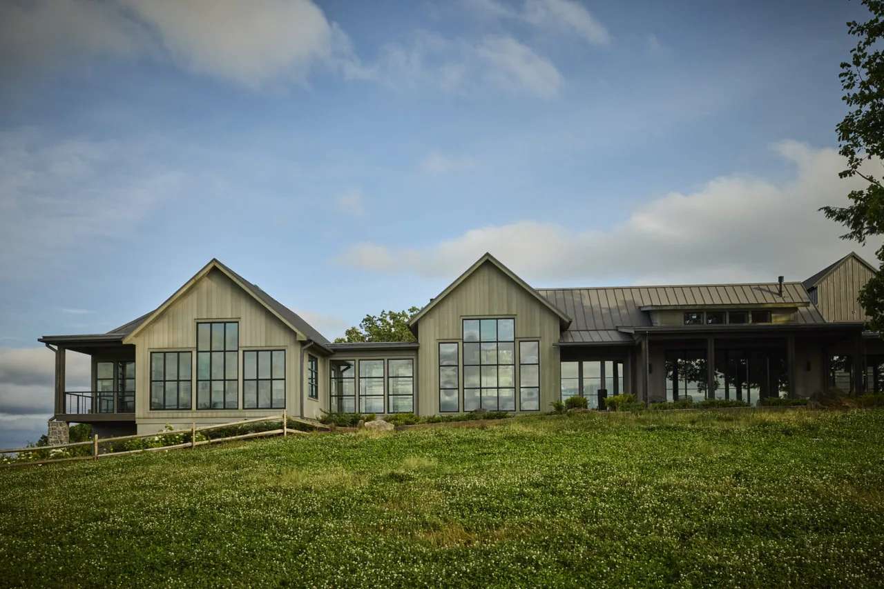Modern farmhouse exterior with large black window frames and a metal gable roof set on a grassy landscape.