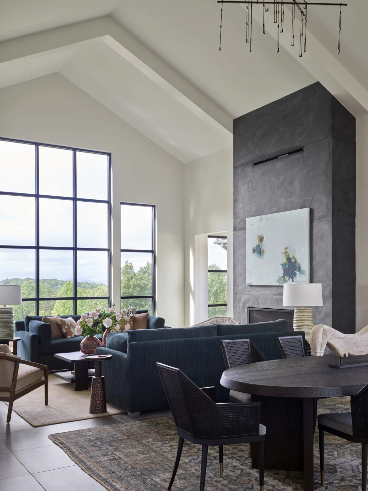 The mountain lake renovation living room features a vaulted ceiling, large black window frames, and a prominent dark stucco fireplace.