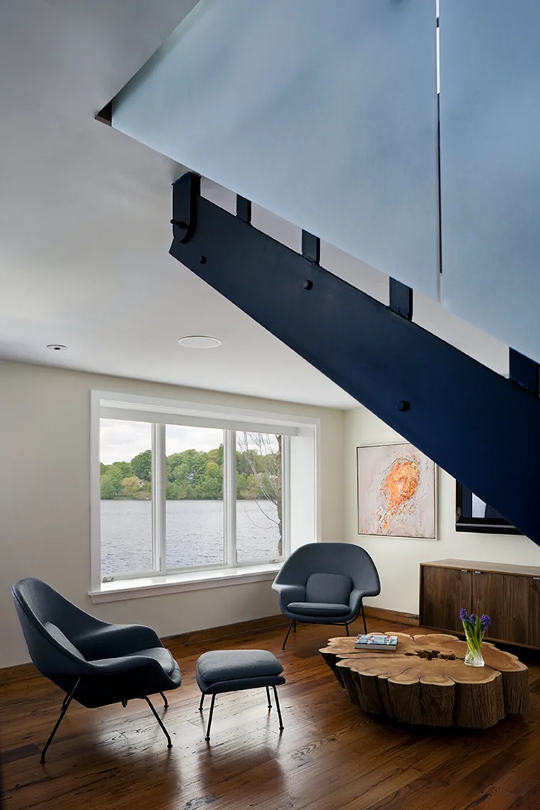 The lake house living area features modern armchairs and a natural wood coffee table with a view of the water.