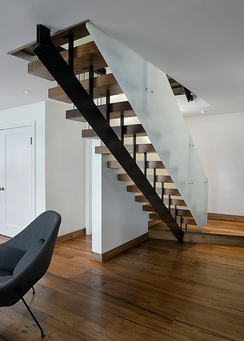 Floating staircase with wood treads, black metal stringer, and frosted glass railing at Connecticut Lake House interior.