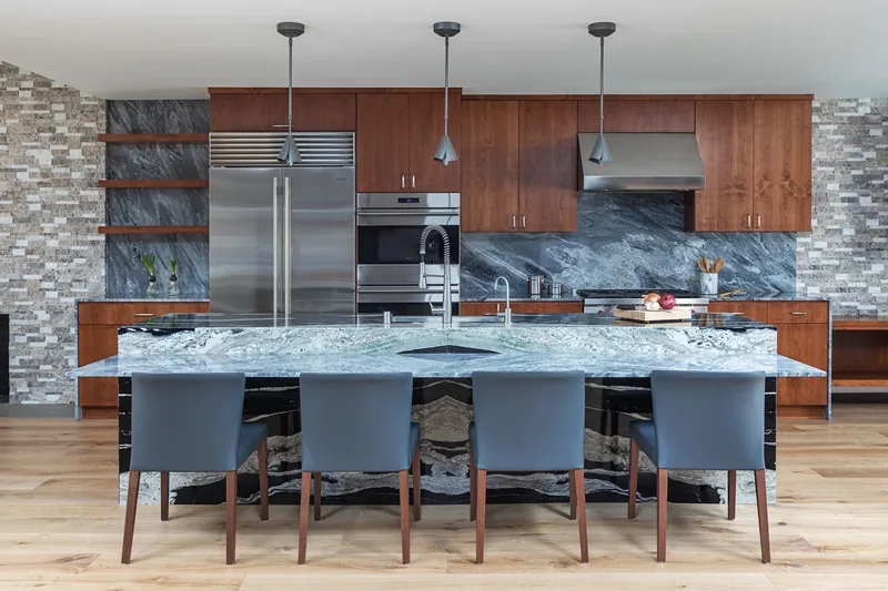 Gray project kitchen by Jeannette Architects features a marble island and wood cabinetry with stainless steel appliances.