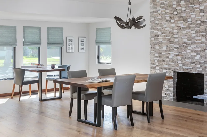 Dining room with wood table and stone fireplace, featuring five windows with Roman window shades.