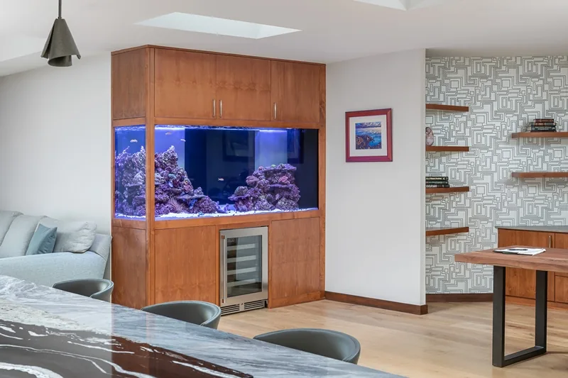 Open area featuring a built-in aquarium with a wine cooler below and floating wooden shelves on a geometric patterned wall.