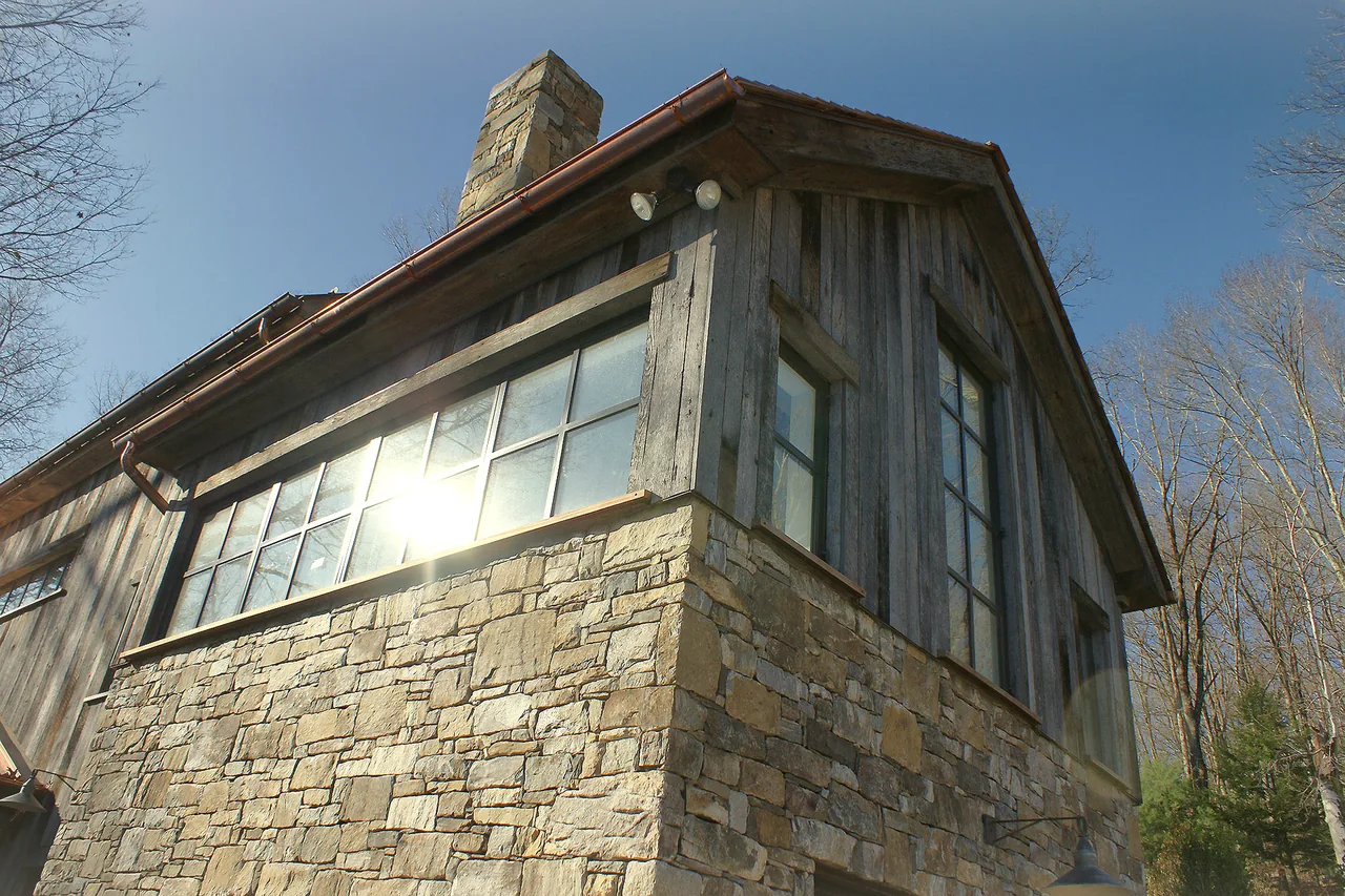 Exterior corner of ROXBURY HOUSE features stone masonry with vertical wood siding and a tall stone chimney.