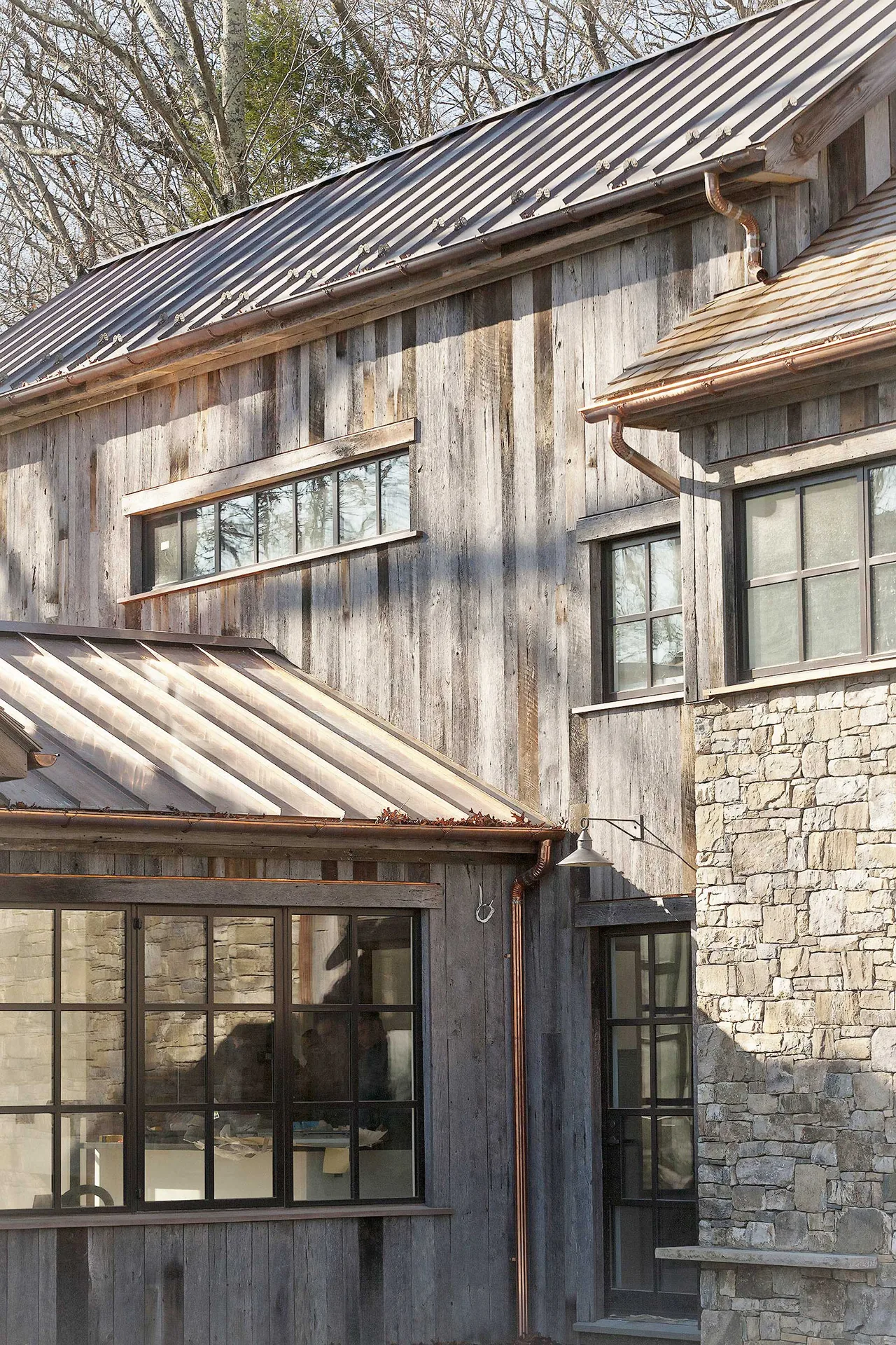 Roxbury House exterior features weathered wood siding, stone walls, large multi-pane windows, and metal roofing.