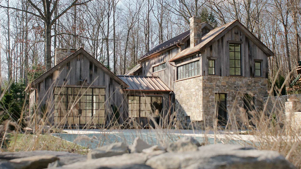 The Roxbury House by Jendretzki LLC features weathered wood siding, large multi-pane windows, and stone elements with copper gutters on a metal roof.