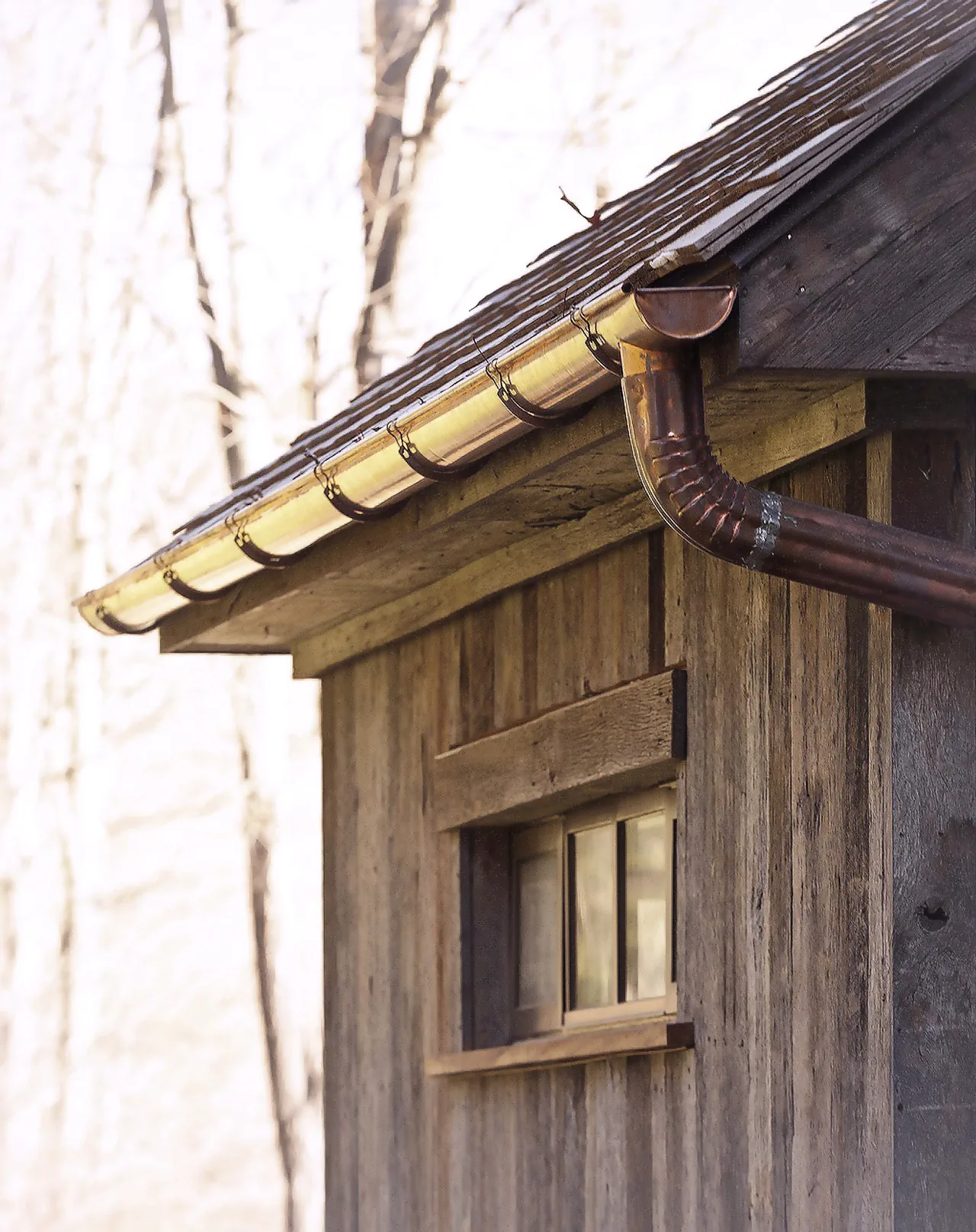 Corner detail of a wood-sided building with copper gutters and a horizontal multi-pane window.
