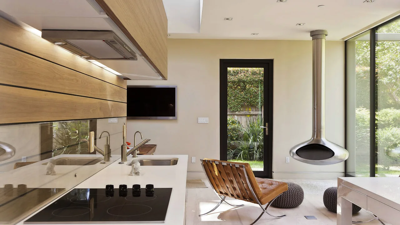 Open kitchen and living area with wood cabinetry, induction cooktop, and hanging fireplace next to glass door to garden.