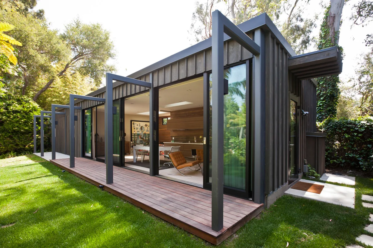 The Santa Monica Pavilion features folding glass doors with black steel frames opening to a narrow wooden deck in a lush garden setting.