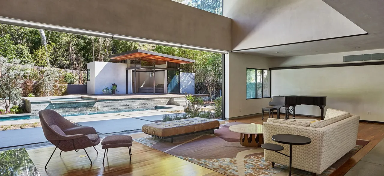 Living room with low-profile sofa, grand piano, and sliding glass doors opening to a pool and deck area.