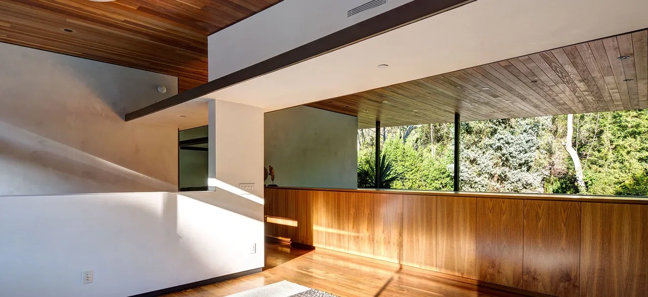 Living room with wood ceiling slats and large rectangular windows framing a green landscape.
