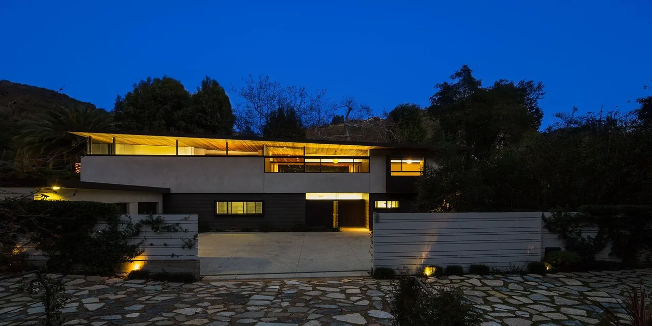 Tree House by Jessie Bornstein features a modern two-story facade with illuminated upper-level windows at night.