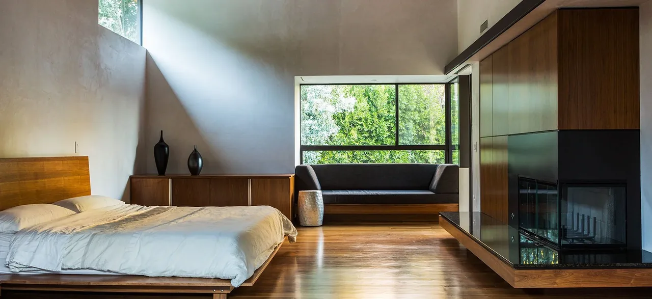 Tree House bedroom features wood floors, a minimalist wood bed, built-in bench seating, and a fireplace with black and wood surround.