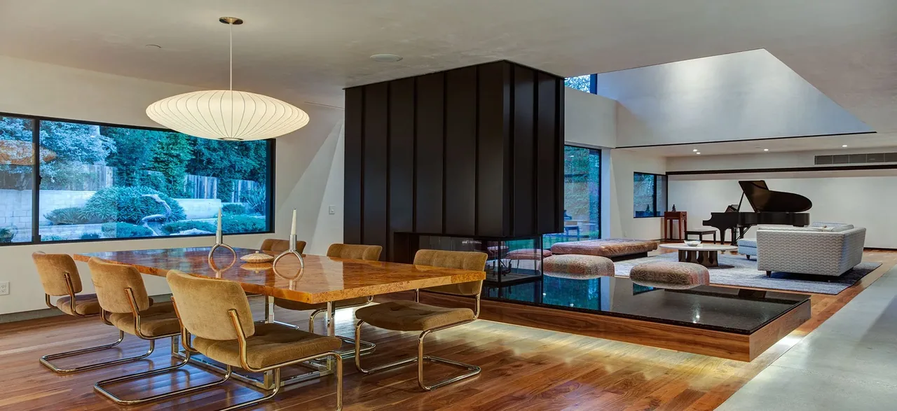 Open living and dining space featuring floor-to-ceiling glazing, a central modern fireplace, and a grand piano.
