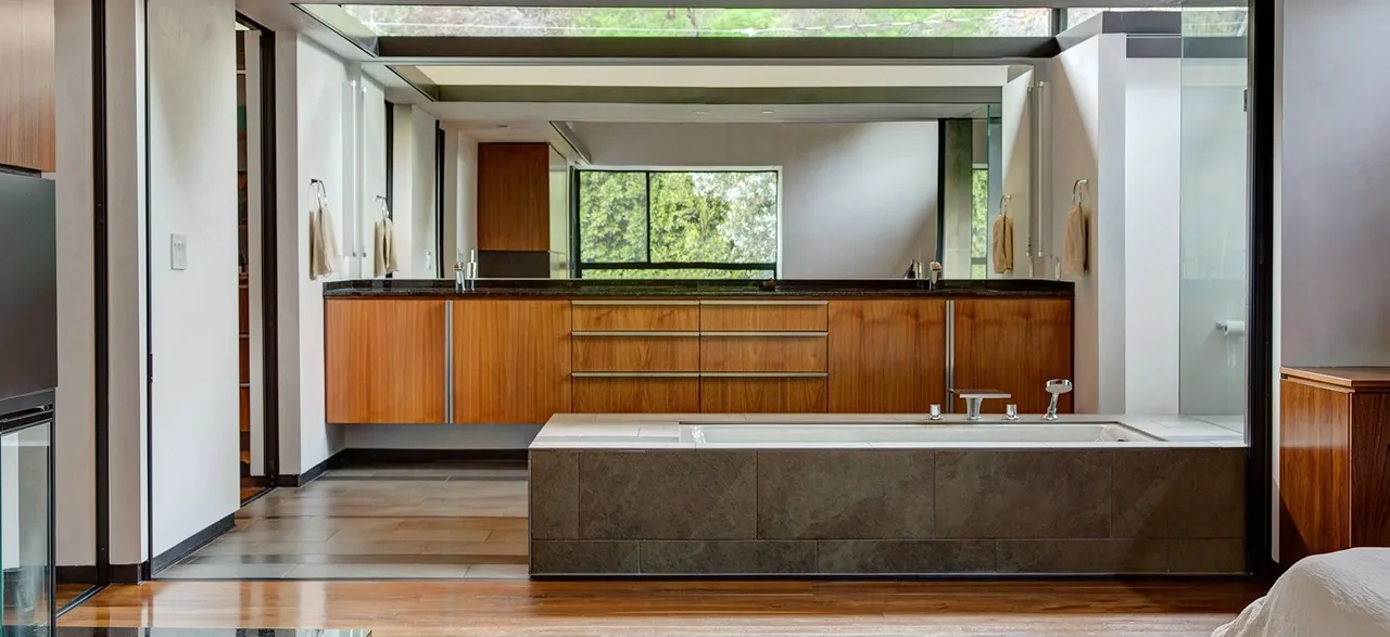 Bathroom features wood cabinetry, a built-in bathtub with tile surround, and a large mirror above the vanity.