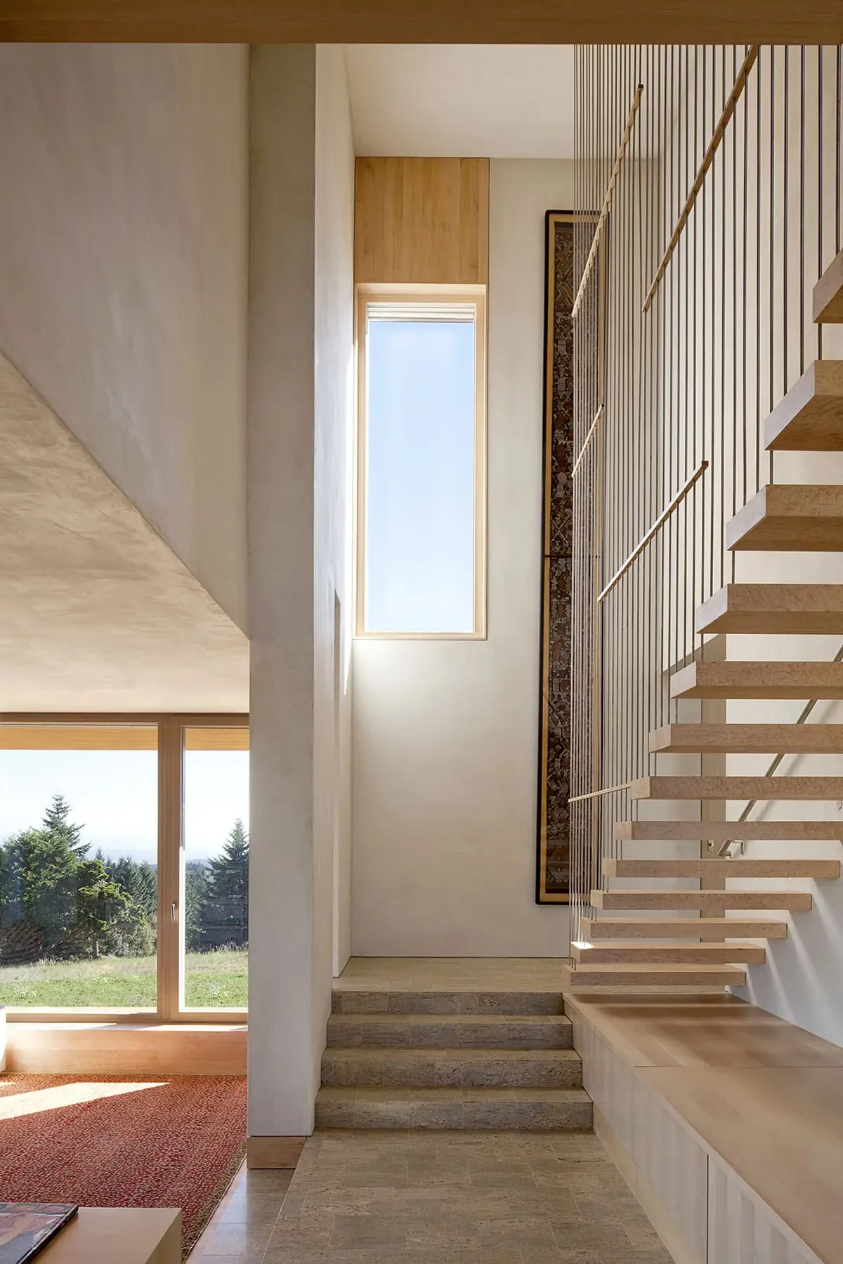 Modern stairwell featuring floating wood steps and a large narrow window for natural illumination.
