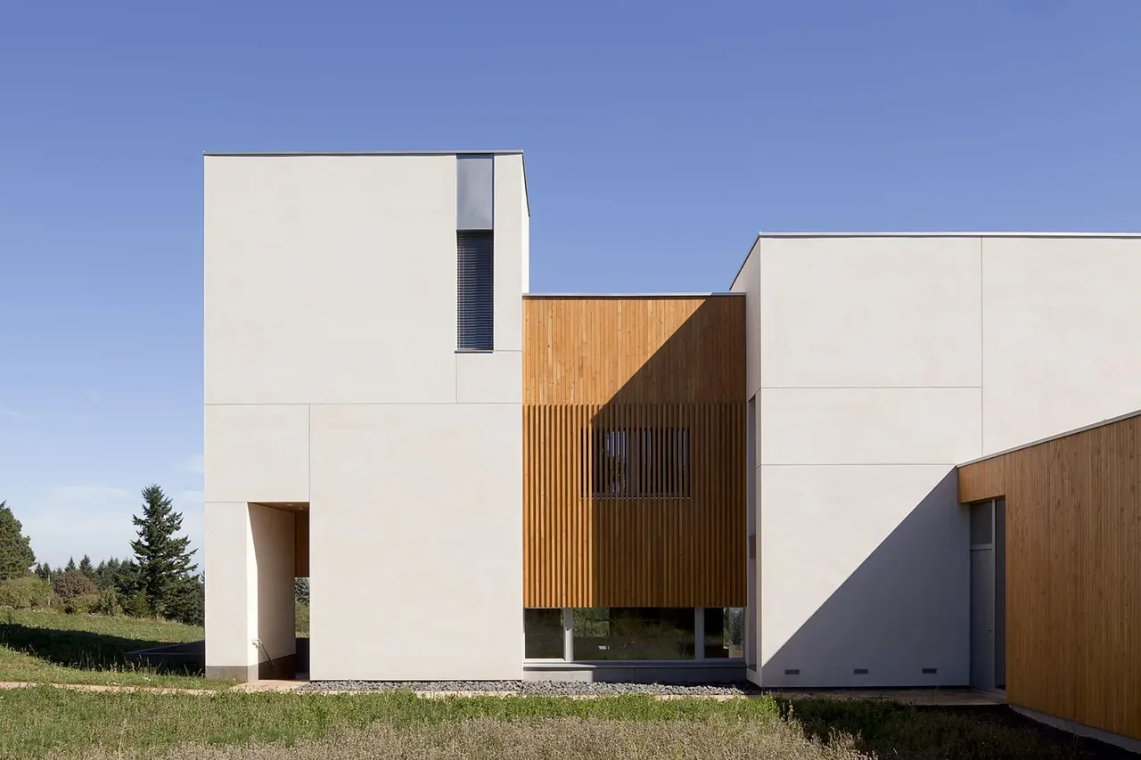 Karuna House features a clean modern exterior with flat roofs and a mix of white stucco and wood siding.