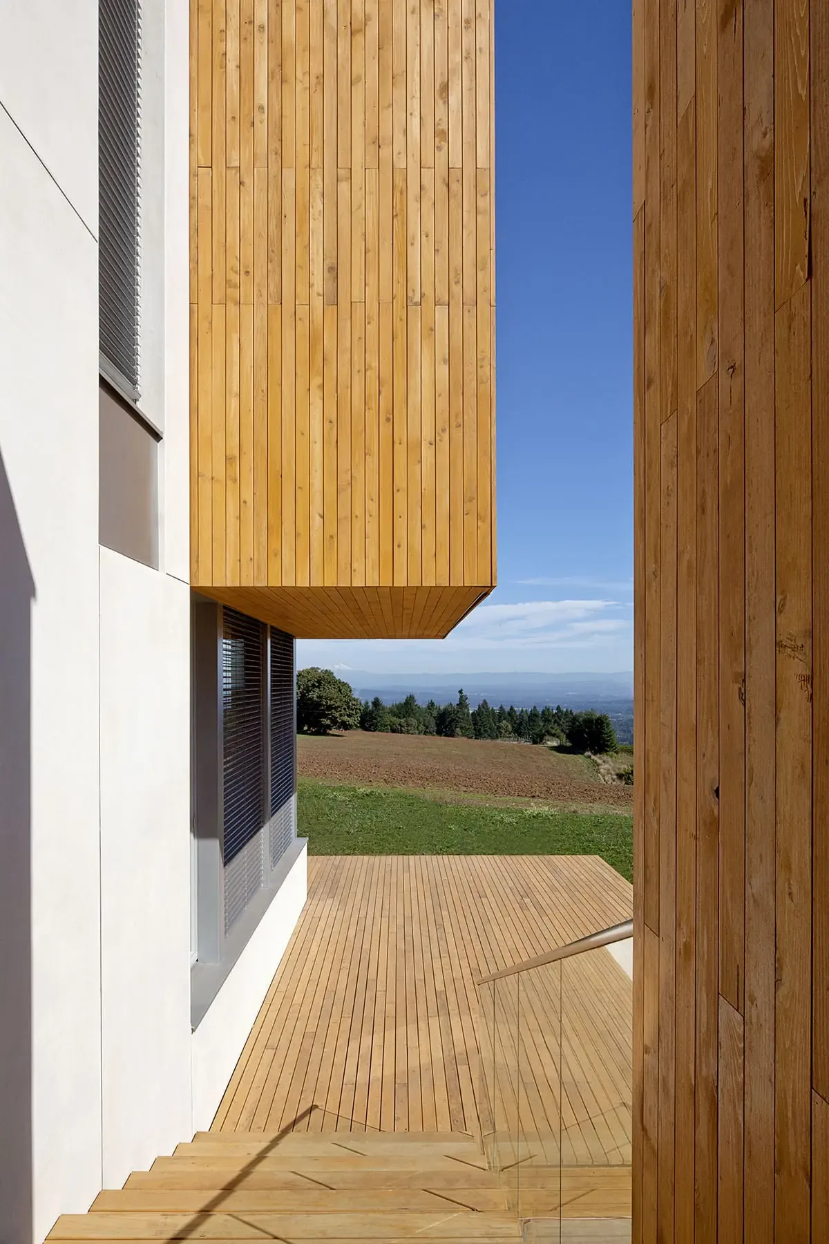Exterior deck area with vertical wood siding and glass railing at Karuna House by Holst Architecture.