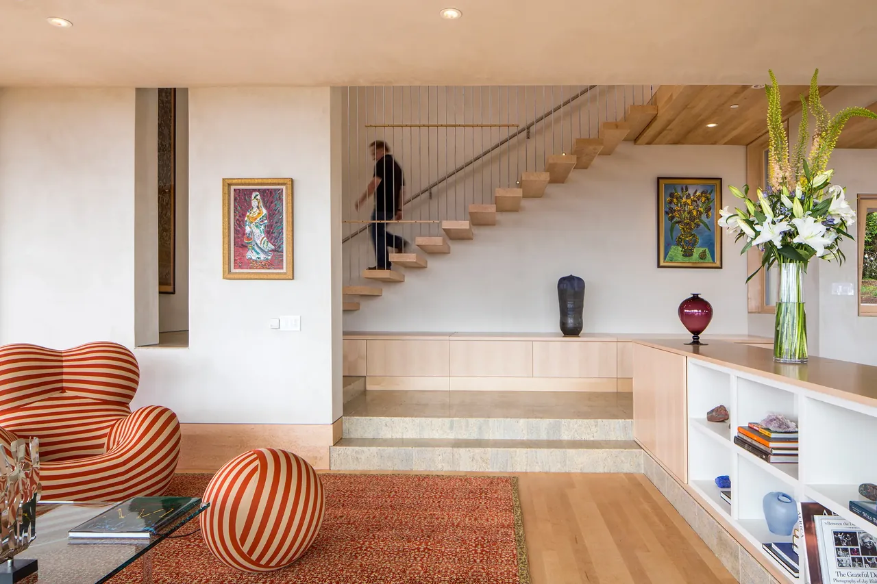Modern living room with a floating wood staircase, artistic decor, and striped furniture in Karuna House.