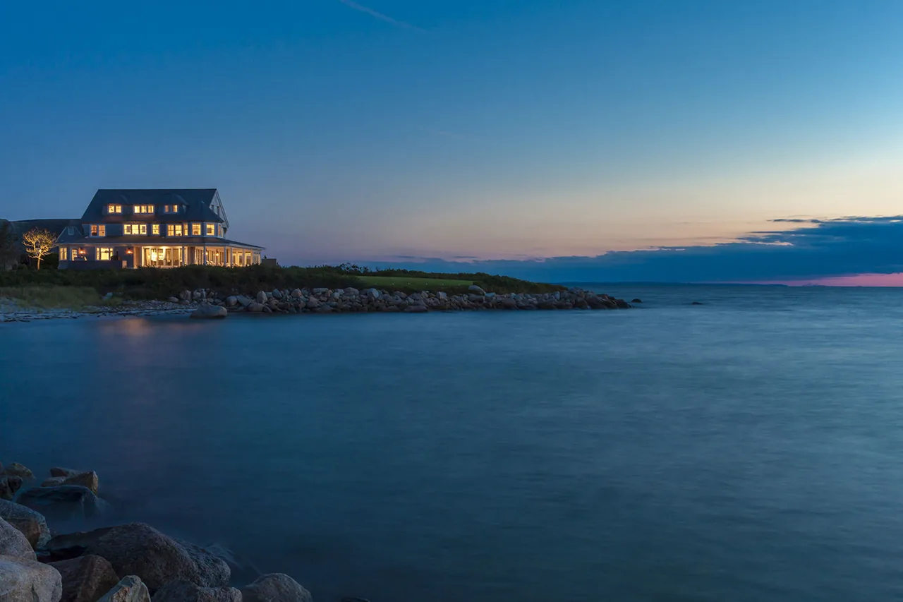 West Bend Point house by Hutker Architects illuminated at dusk on a rocky coastal shoreline.