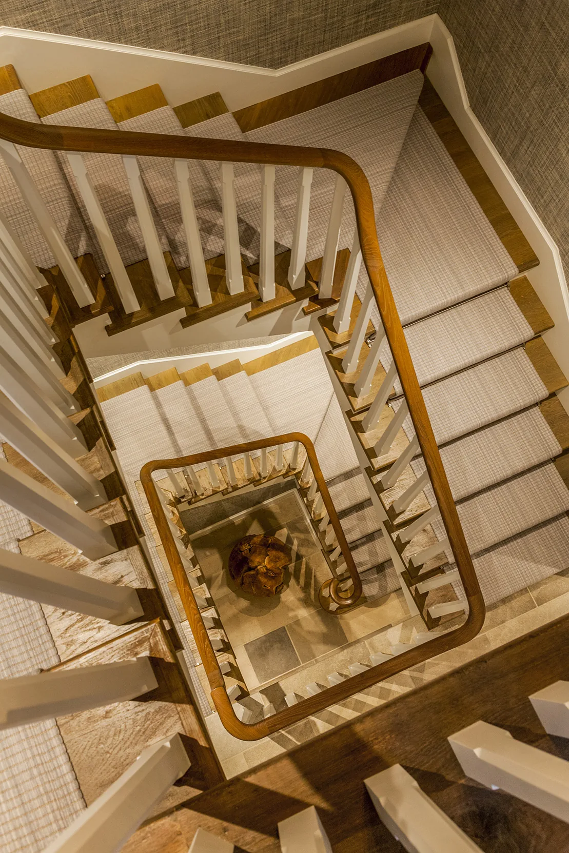 Interior view down a wooden staircase with white balusters and a plaid runner carpet.