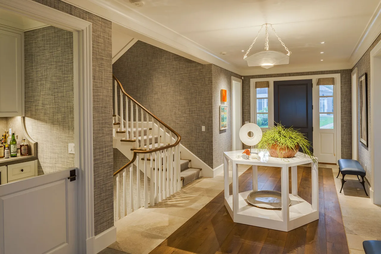 Entry hallway featuring a central display table, staircase with carpeted steps, and dark front door with sidelights.