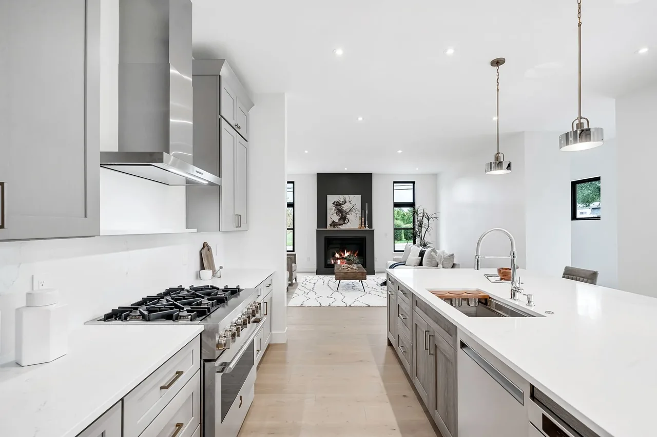 Modern kitchen features a large island, stainless steel appliances, and a living room with a fireplace and black accent wall.