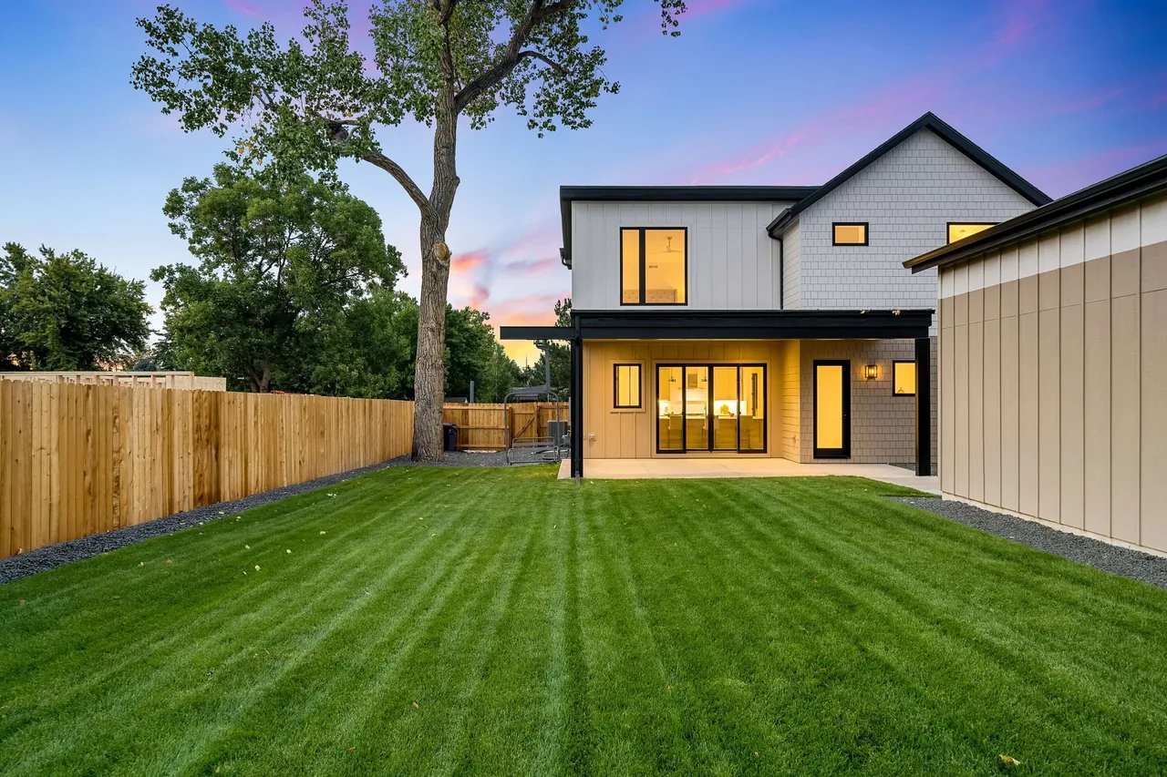 Two-story home featuring a covered patio with sliding doors overlooking a green lawn and wooden fence.