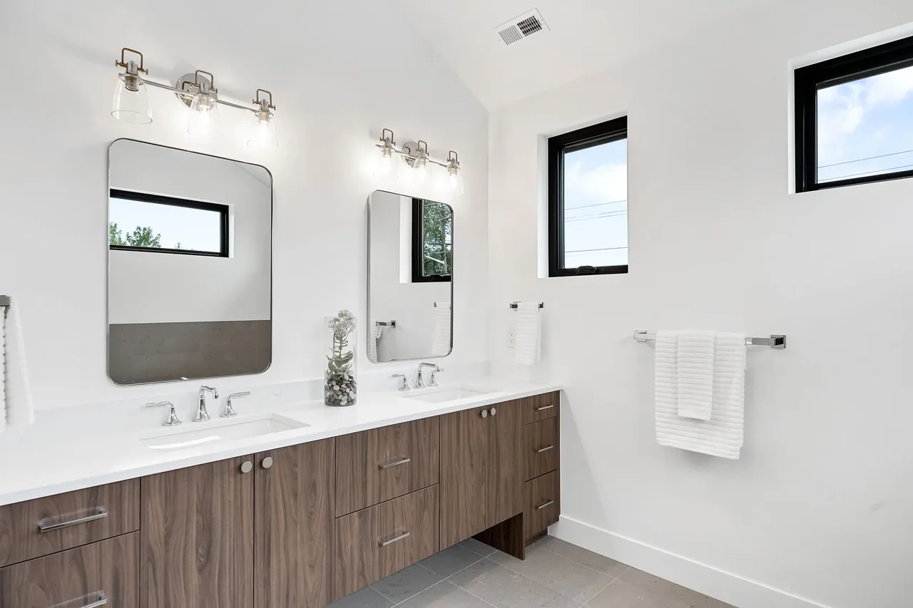 A modern bathroom featuring a double vanity with wood finish and rectangular mirrors above each sink.
