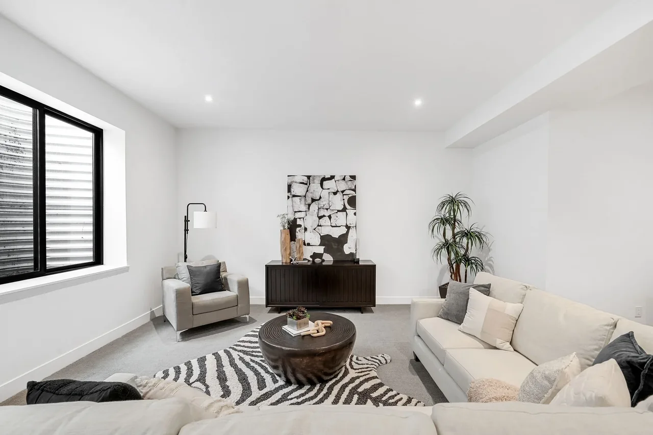 Modern living room featuring a beige sofa and armchair, round wooden coffee table, and black window frames.