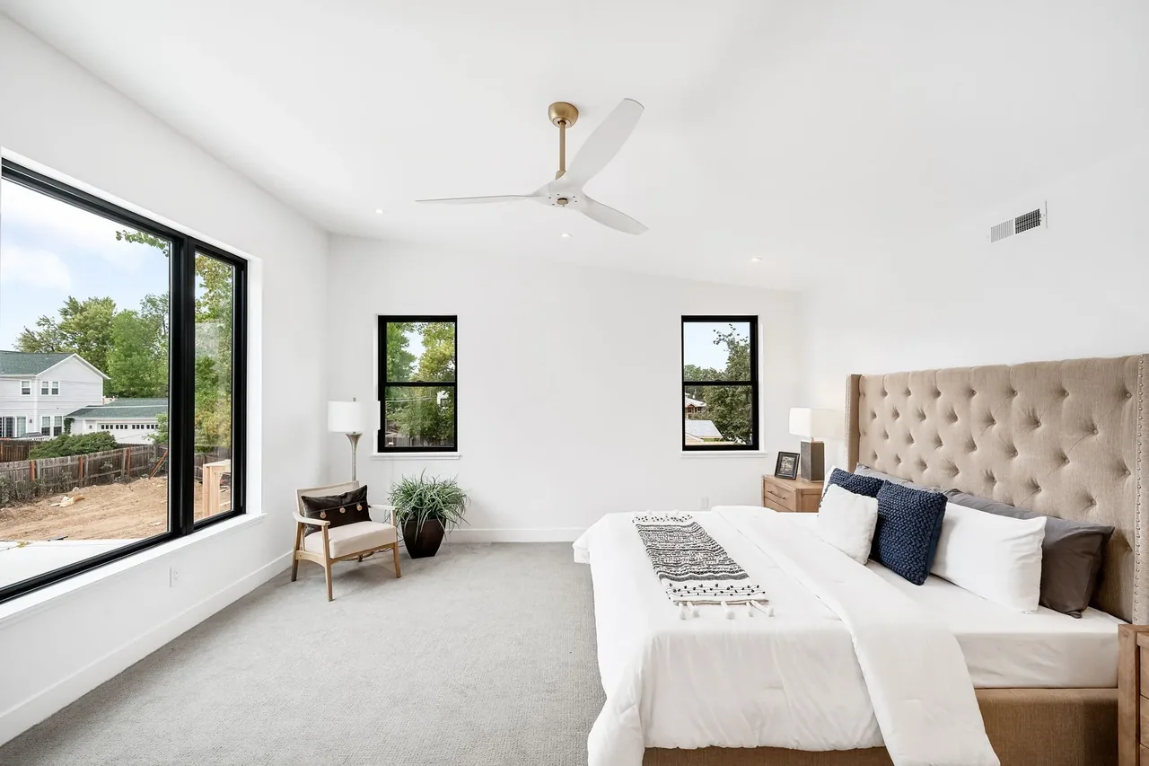 Bedroom with black window frames and tufted bedhead featuring neutral decor and modern ceiling fan.