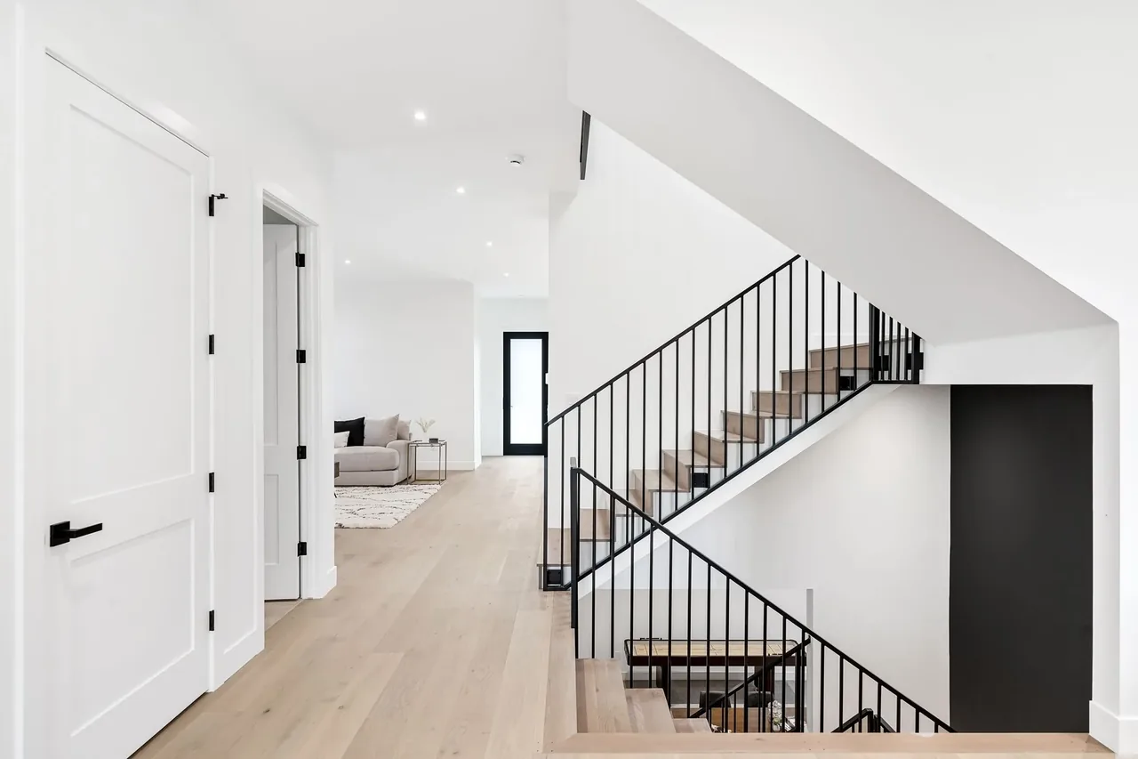 Interior hallway features light wood flooring, white walls, and black metal stair railings.
