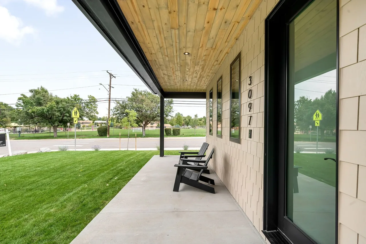Front porch of 3097 S Dexter Way features a concrete floor, wood-paneled ceiling, and black-framed windows and door.
