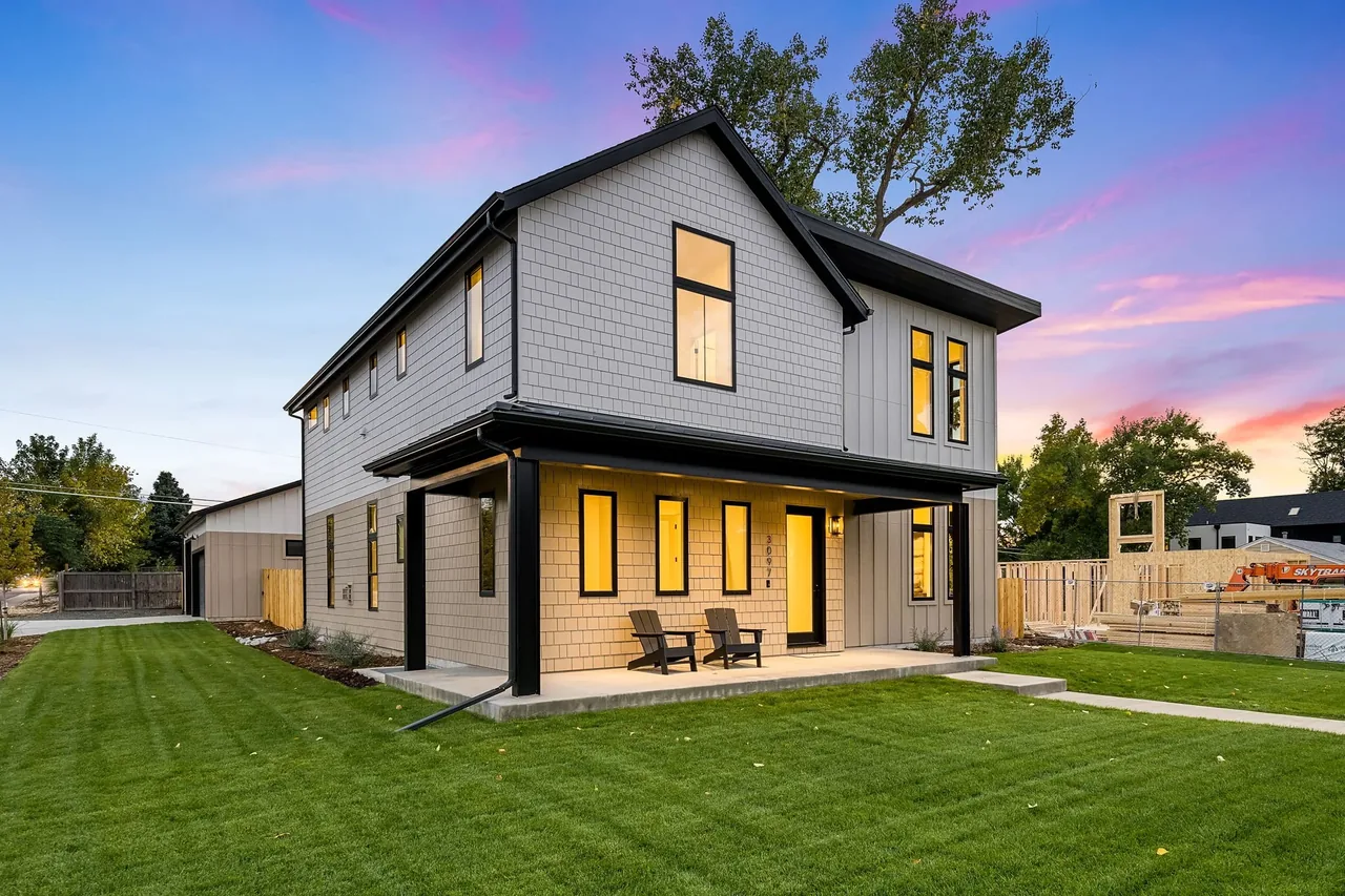 A modern two-story home features shingle and vertical siding, black window frames, and a covered front porch with seating.